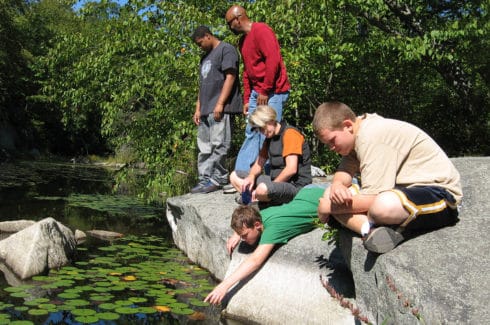 Students and teachers perched on rocks by the side of a river