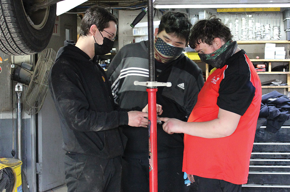 As part of vocational education, Green Chimneys School students are working at local businesses. This image shows 3 individuals under a car at Brewster Shell, two of whom are Green Chimneys students.