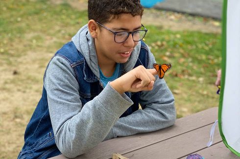 Green Chimneys students sits at a table outdoors and looks at the butterfly perched in his finger.