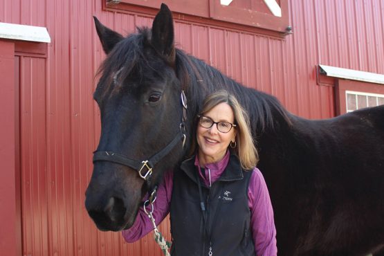 Image of Green Chimneys Board Member and Honoree Michele Greenburg with a large horse in front of a red barn