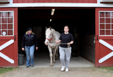 Student Zoe walks her horse partner Gandalf out of the horse barn during a specialized therapy small group session of Hoof Harmony