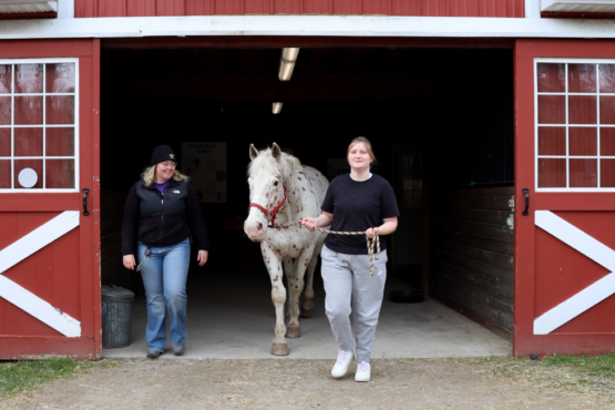 Student Zoe walks her horse partner Gandalf out of the horse barn during a specialized therapy small group session of Hoof Harmony