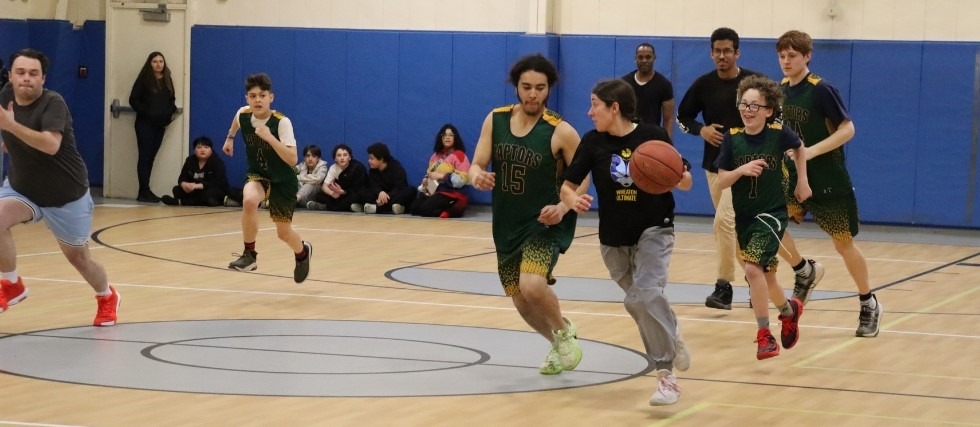 Assistant Residential Supervisor Madeline runs with a basketball down the court as a Green Chimneys student chases with a smile on his face.