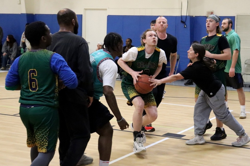 Green Chimneys students and staff gather around a student who is about to shoot the basketball.
